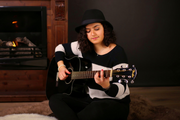 Künstlerfoto: Zara Akopyan Foto der Künstlerin Zara Akopyan mit ihrer Akustikgitarre, sitzend vor einem Kamin.